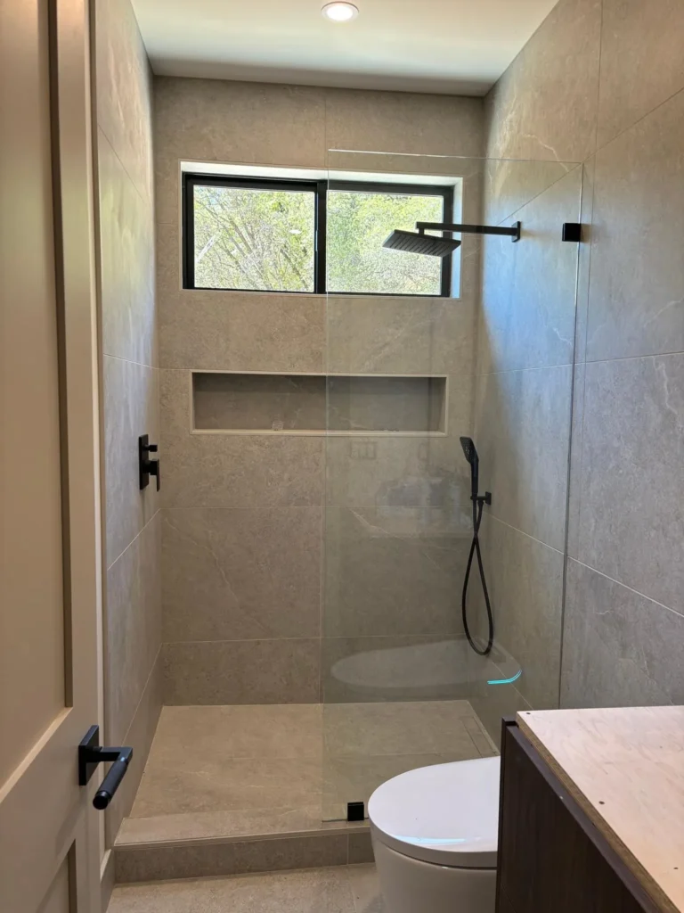 Tiled walk-in shower with a window and matte black fixtures, remodeled by DC Home Renovations in Los Angeles.