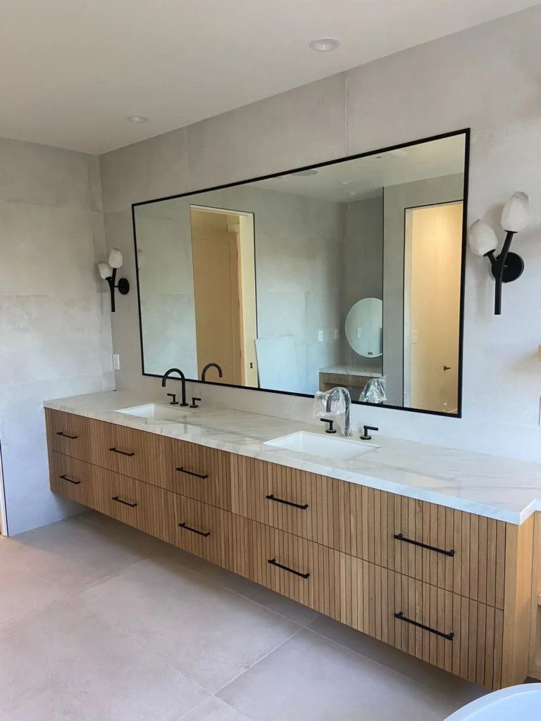 Bathroom with a wood double vanity, large mirror, and marble counters, remodeled by DC Home Renovations in Los Angeles.