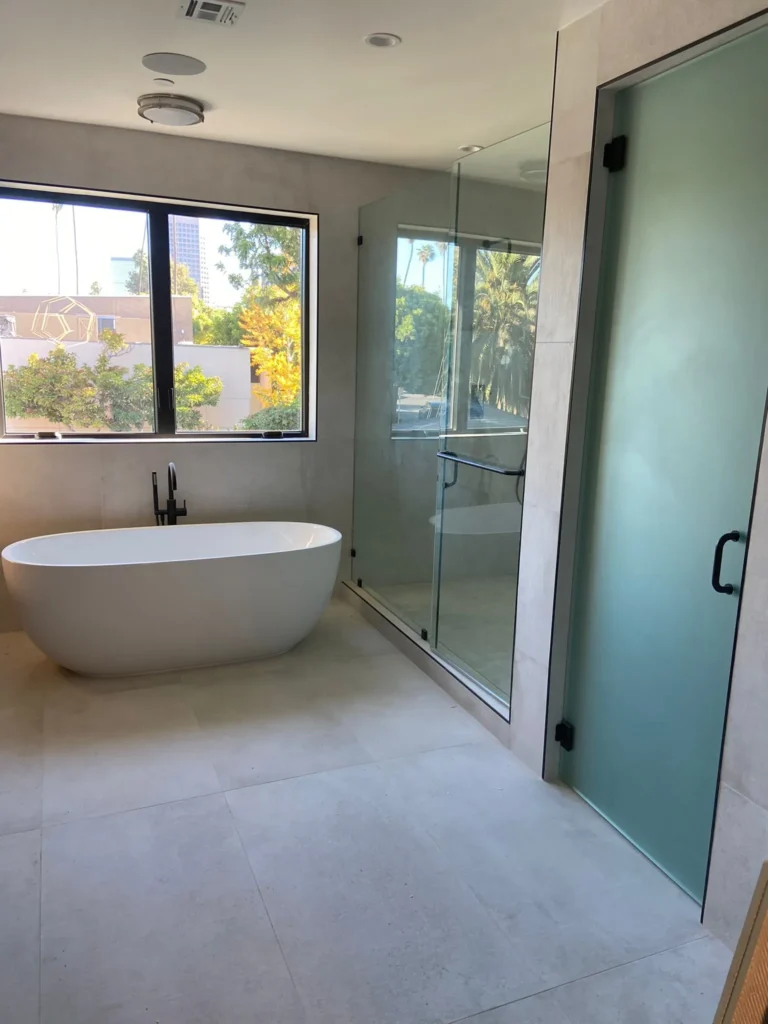 Bathroom with a freestanding tub and a glass walk-in shower by a window, remodeled by DC Home Renovations in Los Angeles.