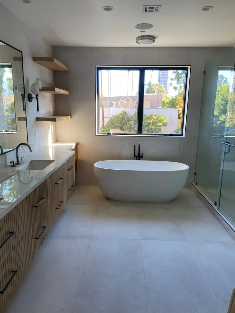 Bright bathroom with a freestanding tub, double vanity, and open shelving, remodeled by DC Home Renovations in Los Angeles.
