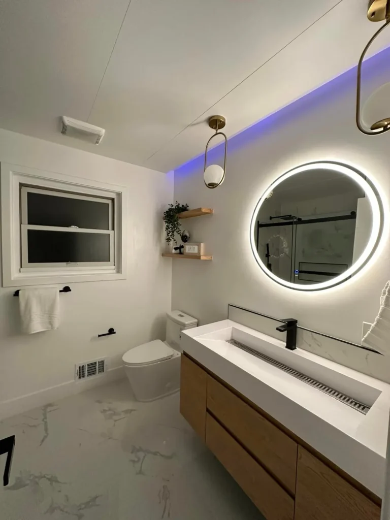 Bathroom with a round backlit mirror, floating wood vanity, and marble counters, remodeled by DC Home Renovations in Los Angeles.