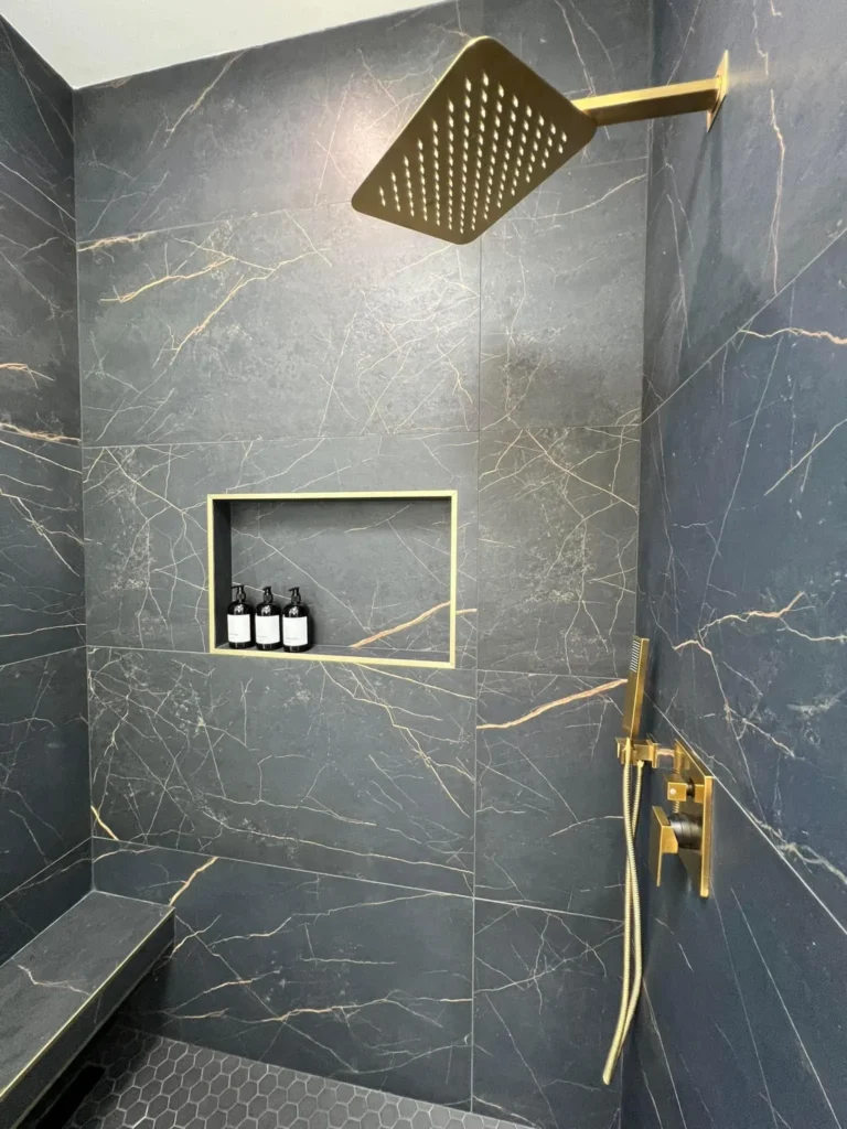 Walk-in shower with a dark marble surround and a gold rain shower head, remodeled by DC Home Renovations in Los Angeles.