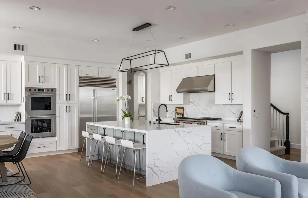 Open modern kitchen with white cabinets, a marble waterfall island, and bar seating, remodeled by DC Home Renovations in Los Angeles.