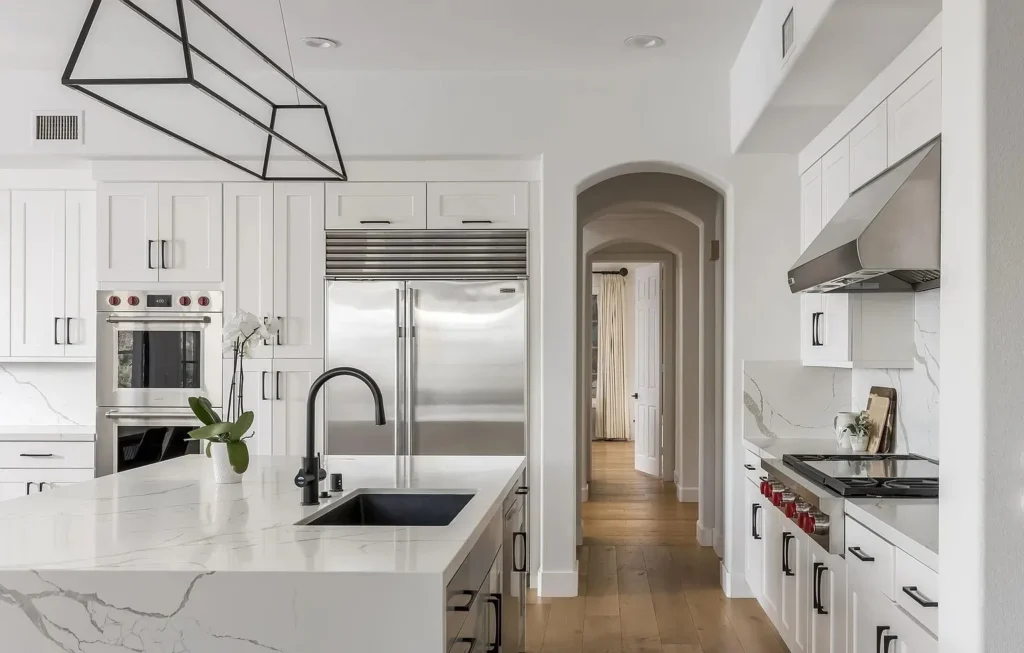 Bright white kitchen with a marble island, stainless refrigerator, and geometric pendant light, remodeled by DC Home Renovations in Los Angeles.