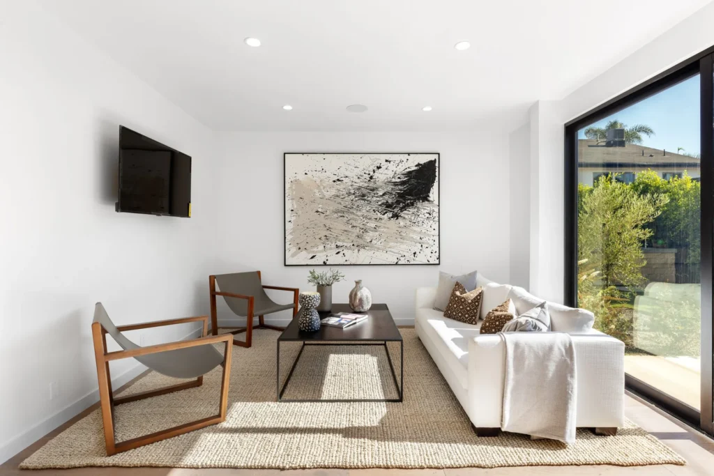 Staged modern living room with a large window, neutral sofa, and framed art, remodeled by DC Home Renovations in Los Angeles.