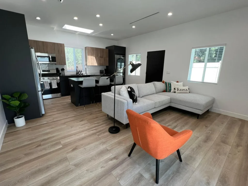 Open-concept living room and kitchen with dark cabinetry and a bright accent chair, remodeled by DC Home Renovations in Los Angeles.